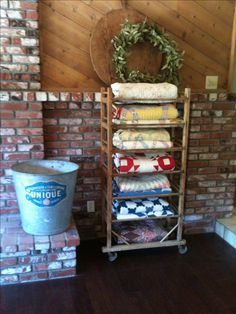 a stack of blankets sitting on top of a wooden shelf next to a bucket and brick wall