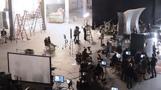 a large group of people in a room with lights and cameras on the floor, behind them are laptops