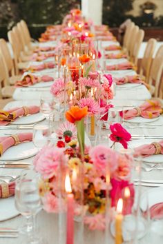 a long table is set with pink and orange flowers, candles, and napkins