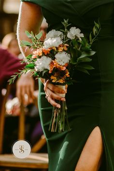 a woman in a green dress holding a bouquet of white and orange flowers on her arm