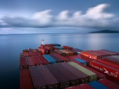 a large body of water filled with lots of red shipping containers under a cloudy sky