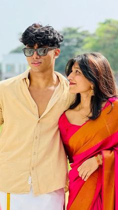 a man standing next to a woman in a pink and orange sari on the beach