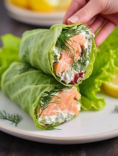 a person is picking up some lettuce wrapped in salmon on a plate with lemon wedges