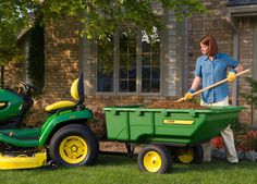 a man is pushing a green wagon with a yellow handle and two large shovels