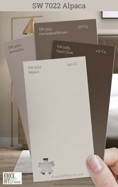 a hand holding three different shades of brown and white paint swatches with the words sw 7022 alpaca on them