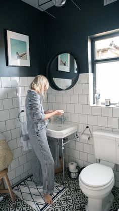 a woman standing in a bathroom next to a white toilet and sink with the lid up