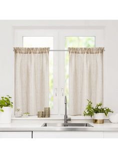 a kitchen window with curtains and potted plants