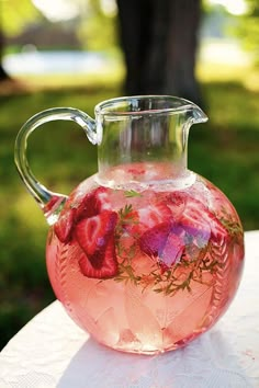 a pitcher filled with water and strawberries on top of a white tablecloth covered table