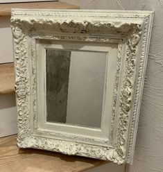 an ornate white framed mirror sitting on top of a wooden shelf next to some stairs