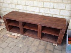 a wooden bench sitting on top of a brick floor next to a trash can and bin