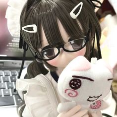 a girl with glasses holding a stuffed animal in front of a computer keyboard and mouse