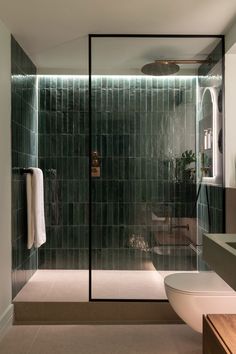 a bathroom with a glass shower door next to a white toilet and bathtub in front of a green tiled wall