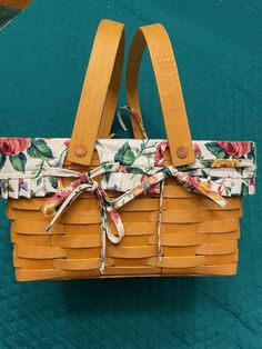 a woven basket with floral fabric tied to the handle and handles, sitting on a green surface