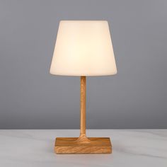 a wooden table lamp with a white light on it's base and a grey background