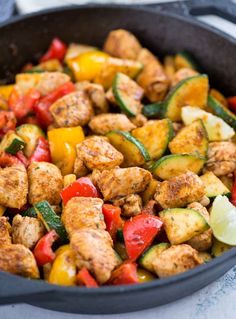 a skillet filled with chicken, peppers and zucchini on top of a table