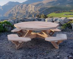 a wooden picnic table sitting on top of a gravel field next to a lush green hillside