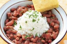 a white bowl filled with beans and rice next to a piece of bread on top of a table