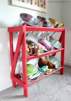 a red rack with bowls and pans on it in front of a white wall