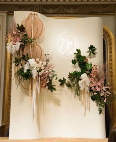 flowers and greenery are arranged on the wall in front of an ornate gold frame