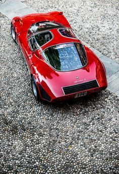 a red car parked on top of a gravel covered parking lot next to a tree