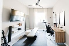 a room with a desk, chair and television on the wall next to a window