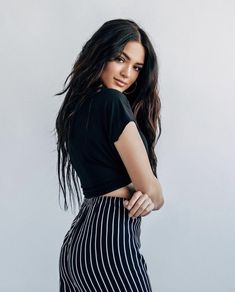 a woman with long dark hair wearing a black top and striped skirt posing for the camera