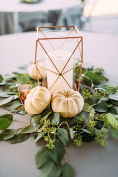 pumpkins and greenery are arranged on a table with a candle holder in the middle