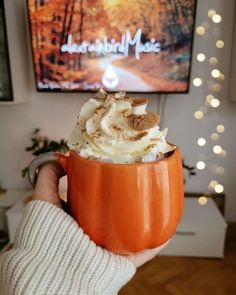 someone holding up a pumpkin mug with whipped cream in it