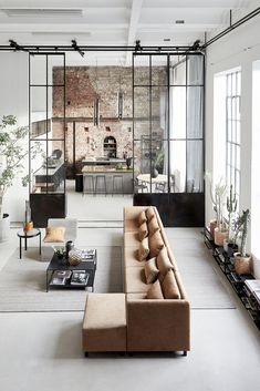 a living room filled with furniture and lots of windows next to a brick wall covered in plants