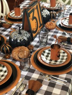 the table is set with black and white checkered cloth, pumpkins, silverware, candlesticks