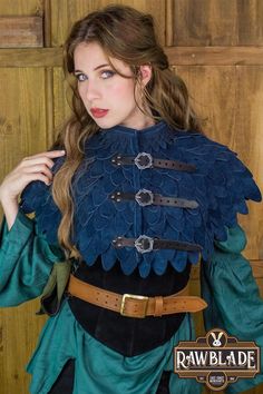 a woman wearing a blue and black outfit with feathers on her shoulders, standing in front of a wooden door