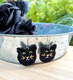 two black cats with yellow eyes are sitting in a metal bowl next to a rose