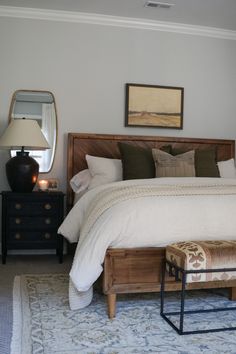 a bedroom with a bed, dresser and mirror on the wall next to an ottoman