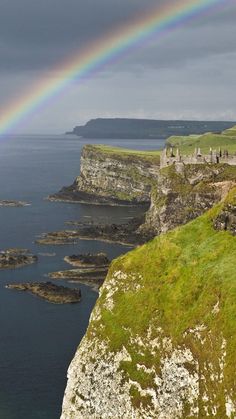 a rainbow shines in the sky over an island with cliffs and grass on either side