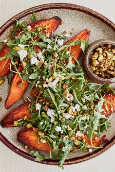 a plate topped with carrots and greens next to a small bowl filled with nuts