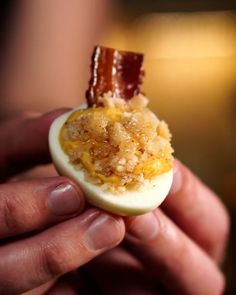 someone holding an egg with bacon on it and some other things in the shell to eat