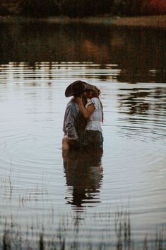 a man and woman kissing in the middle of a body of water with tall grass around them