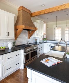 a kitchen with white cabinets and black counter tops, an oven hood over the stove