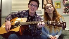 a man and woman sitting on a couch holding guitars in front of the camera,