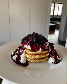 a stack of pancakes with blueberries and whipped cream on top sitting on a white plate