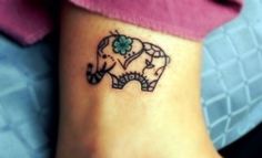 an elephant tattoo on the ankle of a woman's foot with four leaf clovers