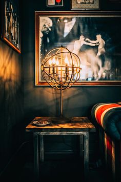 a table with a candle on it in front of a wall with pictures and paintings