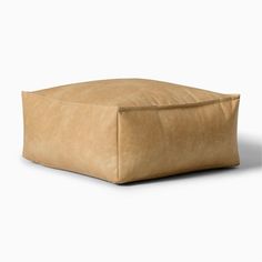 a square leather ottoman that is made out of tan suede fabric and has a rounded, rectangle shaped cushion on the top