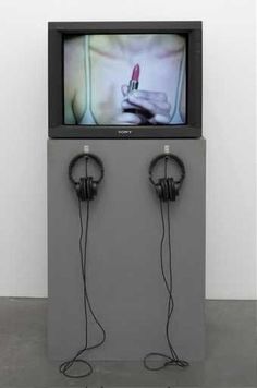 an old television with headphones and a lipstick on the screen is in front of a white wall