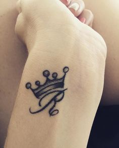 a small tattoo on the wrist of a woman with a crown in her left hand