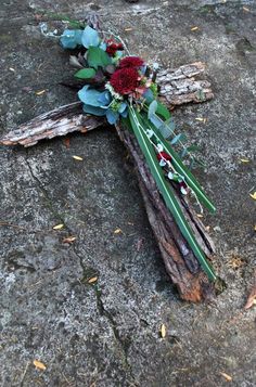 a cross made out of wood with flowers on it sitting on the ground next to leaves