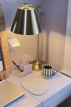 a desk with a lamp, cup and laptop on it next to a mirror in the corner