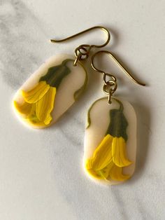 Earrings featuring a kowhai flower. The kowhai flower drop is made from a slice of a polymer clay cane hand made by me. The picture has a translucent background and the flower is visible throughout the slice. Slices are hand shaped, smoothed and hand sanded, then finished with hypoallergenic niobium earwires. Note that because they are hand made, measurements are approximate only. The latest batch has the translucent background with a slightly sepia tone to it - see photos. Earwires are availabl Nature-inspired Green Flower Earrings For Gifts, Green Flower-shaped Nature-inspired Earrings, Handmade Green Flower-shaped Earrings, Botanical Flower-shaped Hypoallergenic Earrings, Unique Flower-shaped Earrings With Pressed Flowers, Polymer Clay Cane, Hand Shapes, Wire Earrings, Ear Wire