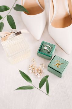 wedding accessories including shoes, ring and jewelry on a white tablecloth with green leaves