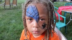 a little boy with his face painted like a spider man on his forehead, sitting in the grass